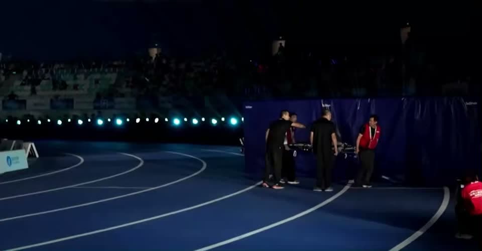 Frame aos 42 s: quatro técnicos carregam um robô numa maca, fora da pista.